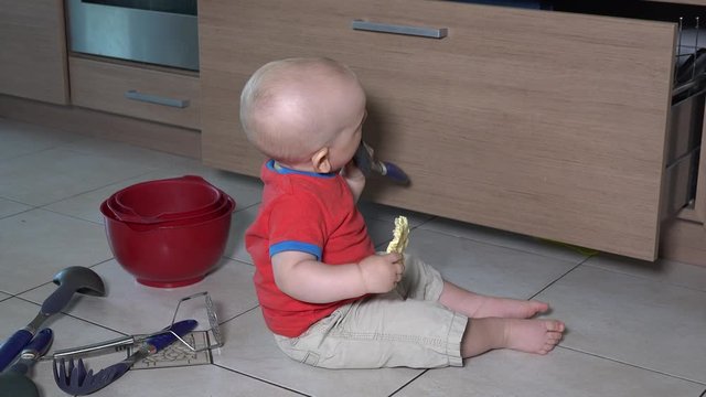 Toddler boy eat food sitting in mess on kitchen floor