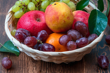 red grape berries and fresh fruits in a straw basket on a dark wooden background.