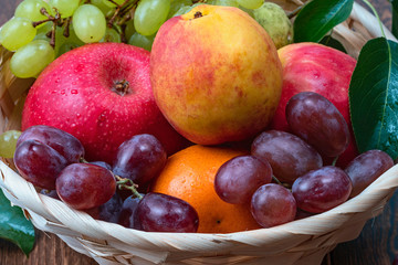 red grape berries and fresh fruits in a straw basket on a dark wooden background.
