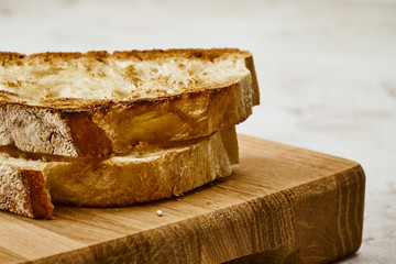 Slices of fried freshly baked bread with a piece of butter on top, lie on a wooden shelf on a marble table