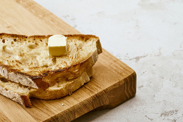 Slices of fried freshly baked bread with a piece of butter on top, lie on a wooden shelf on a marble table