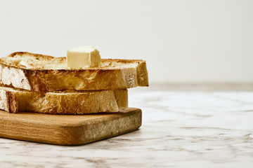Slices of fried freshly baked bread with a piece of butter on top, lie on a wooden shelf on a marble table