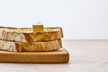 Slices of fried freshly baked bread with a piece of butter on top, lie on a wooden shelf on a marble table