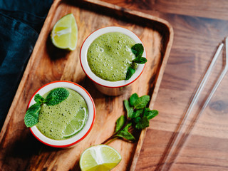 Two portions of green spinach smoothie with banana, lime and oat milk.