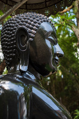 Face and top body part of a peaceful black stone sitting Buddha statue posing “The attitude of...