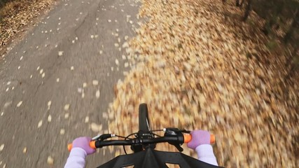 Pov view. One caucasian children rides bike road in autumn park. Little girl riding black orange mtb cycle in forest. Kid goes do bicycle sports. Biker motion ride with backpack and helmet.