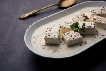 Paneer Dum Kali Mirch / Kalimirch, prepared in a white creamy gravy and black pepper powder sprinkled over it. served in a bowl. Selective focus