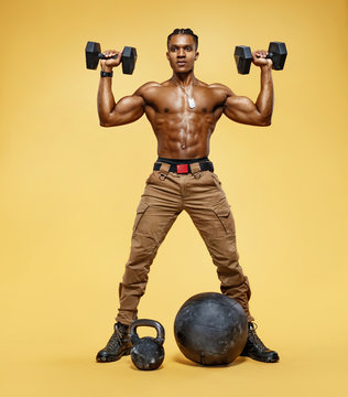 Man doing exercise with dumbbells. Photo of sporty man in training, pumping up muscles on yellow background. Rear view. Full length