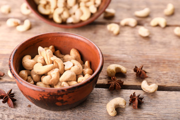 Bowl with tasty cashew nuts on wooden background
