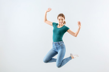 Jumping young woman against light background