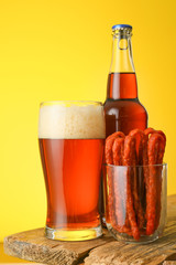 Fresh beer and sausages on table against color background