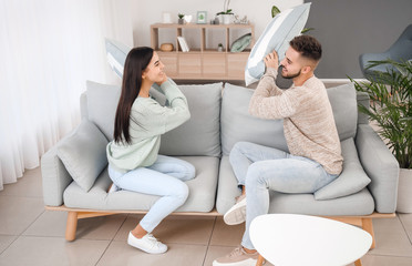 Obraz premium Young couple fighting on pillows while sitting on sofa at home