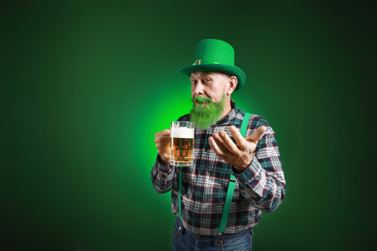 Funny mature man with glass of beer inviting viewer on dark background. St. Patrick's Day celebration