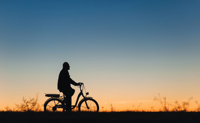 Fototapeta na wymiar Male cyclist on the e-bike or electric bicycle on the sunset background. Silhouette of the man in profile. Active pension. Travel. Sport.