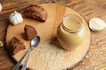 Jar of tasty tahini with bread on wooden table