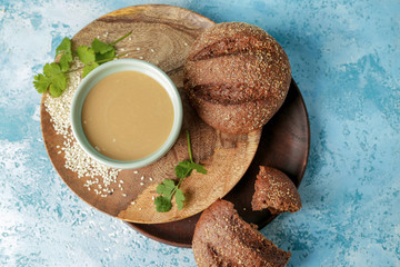 Bowl of tasty tahini with bread on color background
