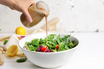 Badezimmer Foto Rückwand Woman pouring tasty tahini from jar onto vegetable salad in bowl © Pixel-Shot