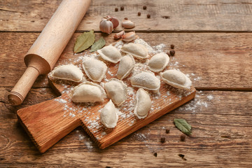 Board with raw dumplings and spices on wooden background