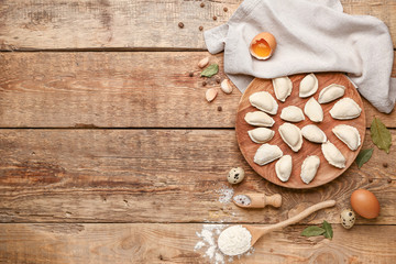 Plate with raw dumplings on wooden background