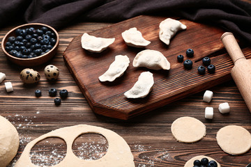 Raw dough and dumplings with ingredients on wooden background