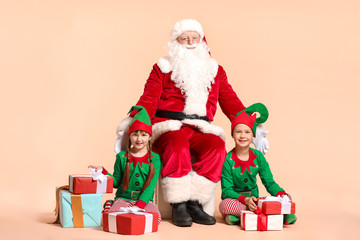 Santa Claus and little elf kids with gifts on color background
