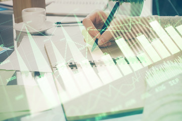 Forex chart hologram on hand taking notes background. Concept of analysis. Double exposure