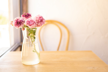 Bouquet of pink roses in glass vase with water on brown wooden table, blurred chair on white background, copy space