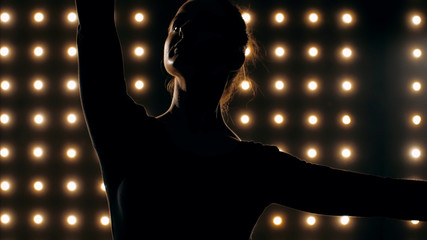 Silhouette of ballerina in black tutu is dancing ballet in the dark studio with smoke and the lights on the background. © alexeg84