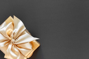 Festive background with gold gift, box with gold ribbon and bow on black background, flat lay, top view,copy space