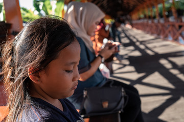 semporna, Malaysia - Nov 27, 2019: Young girl looking tired while sitting on a walkaway in a sunny day.