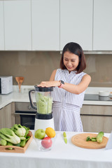 Beautiful Asian Woman juicing making green juice with juice machine in home kitchen. Healthy concept.