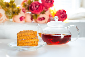 Breakfast concept. Black tea in a glass cup and a teapot on a white table. A slice of honey cake on a transparent saucer. Breakfast for a beloved woman.