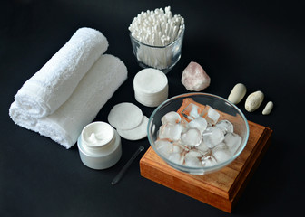 white cotton towels, face cream, cotton pads, sticks, ice cubes, spa on black background