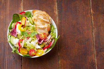 Fresh salad with tomatoes, chicken, bell peppers, radishes and mozarella cheese on wooden background. Top view flatlay with copy space