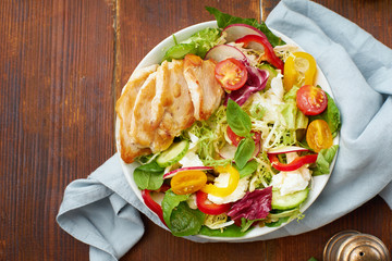 Fresh salad with tomatoes, chicken, bell peppers, radishes and mozarella cheese on wooden background. Overhead image with copy space