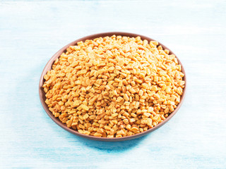 Fenugreek in clay plate on a blue background. Indian cuisine, ayurveda, naturopathy, modern apothecary concept