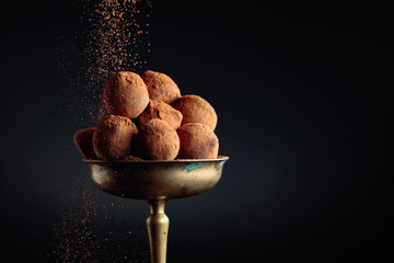 Chocolate truffles in old brass vase sprinkled with cocoa powder.