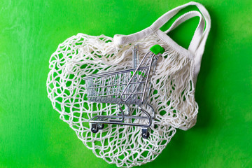 Fototapeta premium small shopping cart over mesh bag on green
