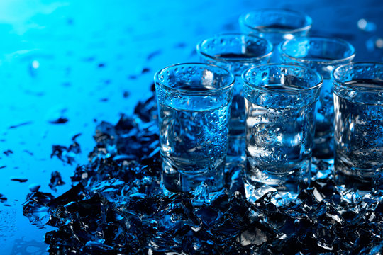 Damp glasses of vodka with ice on a black reflective background.