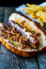 Hot Dog with Caramelized Onion, Cheddar and Gruyere Cheese Sauce on Wooden Surface with Potatoes.