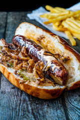 Hot Dog with Caramelized Onion, Cheddar and Gruyere Cheese Sauce on Wooden Surface with Potatoes.