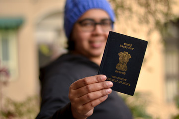 Portrait shot of a young beautiful Indian woman wearing blue cap holding her passport with her face...