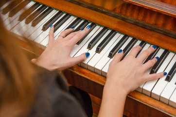 hands of a female pianist with blue nail Polish on the nails on the keys of a piano. girl playing the piano.