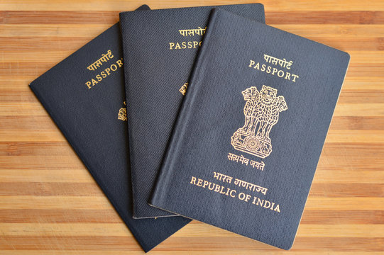 Multiple Indian Passports kept against wooden background on display.  The national emblem of Republic of India is the Lion Capital of Ashoka from Sarnath is embossed on the passport. Global citizen