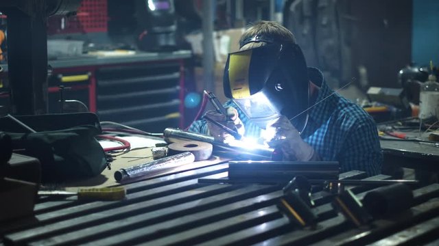 Industrial worker in protective mask using modern machine for welding metal