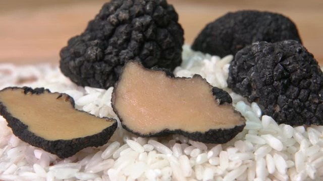 Rare black truffle fungus cutted into pieces on a raw white rice on the wooden board