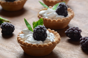 Delicious Tartlets on a wooden Background. Blackberry with cream - dessert.Healthy homemade berry dessert. Close-up of a tartlets with blackberries.
