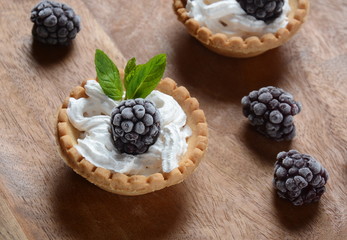 Delicious Tartlets on a wooden Background. Blackberry with cream - dessert.Healthy homemade berry dessert. Close-up of a tartlets with blackberries.