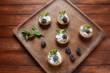 Fototapeta na wymiar Delicious Tartlets on a wooden Background. Blackberry with cream - dessert.Healthy homemade berry dessert. Close-up of a tartlets with blackberries.