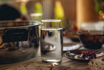 Glass of water on a table full of food, drinks and kitchen objects. Outside dining/meal, sunny day.